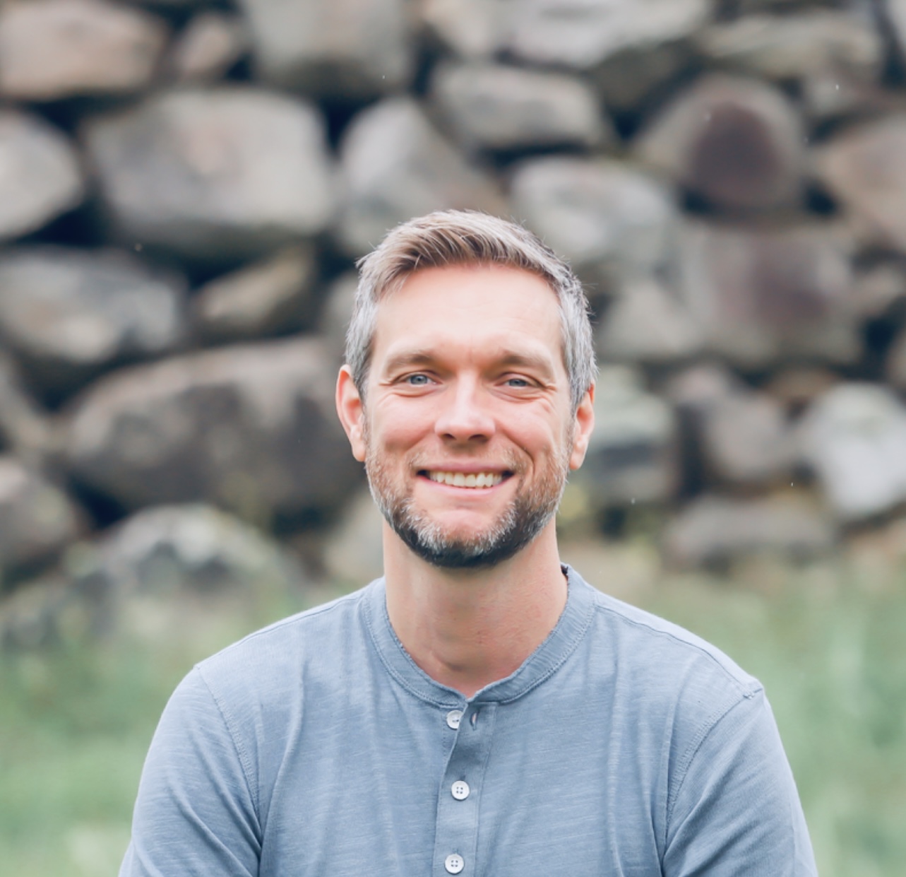 Chris Vail smiling outdoors in front of a natural stone wall